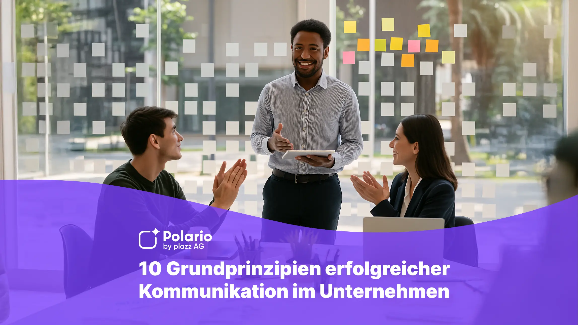 Drei Berufstätige in einem modernen Büro mit Glaswand und bunten Post-its. Ein Mann steht mit Tablet in der Hand und lächelt, während zwei Kolleg:innen ihm applaudieren. Vor ihnen stehen Laptop, Kaffeebecher und Pflanzen auf dem Tisch. Die Szene vermittelt Zusammenarbeit, Wertschätzung und erfolgreiche Teamkommunikation.